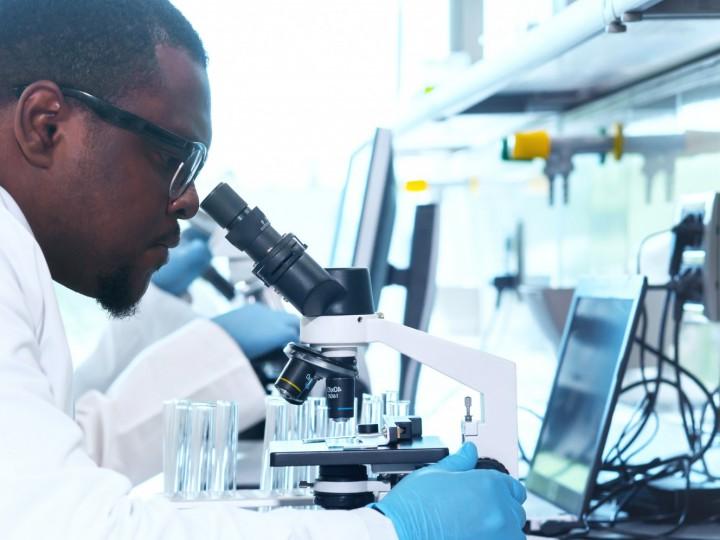 A student wears a labcoat and looks into a microscope during a lab class